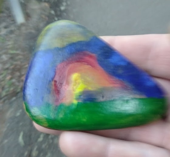rock painted with a rainbow on green grass and blue sky
